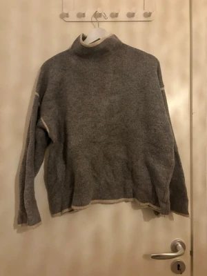 Grå polotröja i ull - Mysig grå polotröja i ull med hög hals och långa ärmar. Tröjan har en loose passform och ljusa detaljer