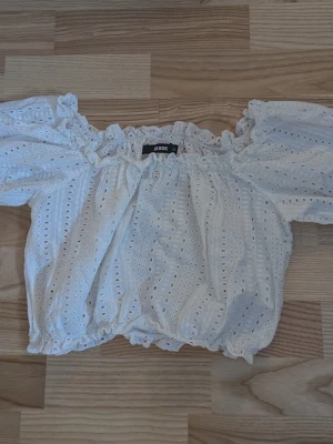 Vit off shoulder blus från Bik Bok - Supersöt vit off shoulder blus från Bik Bok i storlek XS. Blusen har broderade hål, volangkant upptill och nertill samt puffiga korta ärmar Kort i modellen. Perfekt för sommarens alla tillfällen och ger en romantisk vibe.                                                               Pris kan diskuteras vid smidigt köp 😊                        Köparen står för frakt!