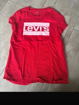 Röd Levi's t-shirt med logga - Snygg röd t-shirt från Levi's med klassisk vit logga framtill. T-shirten har rund hals, korta ärmar och är gjord i mjuk bomull. Perfekt till jeans eller shorts för en chill look.