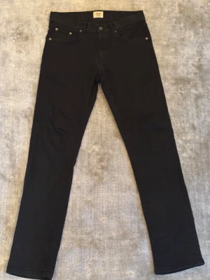 Svarta jeans från East West Baxter - Säljer ett par svarta jeans från East West, modell Baxter Regular Fit. Klassisk femficksdesign, raka ben och normal passform. Jeansen är tillverkade i ett mjukt bomullsmaterial med lite stretch för extra komfort. Perfekta till alla typer av outfits.