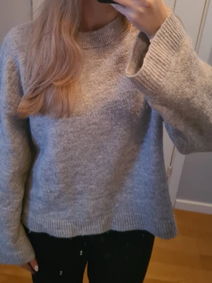 Grå stickad tröja från Gina Tricot - Mysig grå stickad tröja från Gina Tricot i storlek XS. Tröjan har en rund halsringning, ribbade muddar och en loose passform. Perfekt för lager-på-lager under kyliga dagar. Enkel att matcha med både jeans och kjol.