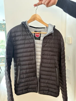 Svart pufferjacka från Colmar - Säljer en svart pufferjacka från Colmar med huva och dragkedja. Jackan har två fickor med dragkedja och en snygg Colmar-logga på ärmen. Insidan är ljusgrå och jackan är lätt vadderad, perfekt för kyliga dagar.