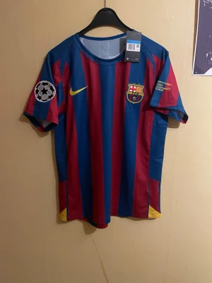 FC Barcelona Ronaldinho #10 – Champions League - En ikonisk FC Barcelona-tröja med Ronaldinho 10 – en hyllning till en av fotbollens största legender. Tröjan är helt ny, oanvänd och med lapp kvar, exakt som på bilderna. Klassiska färger, Champions League-patch och tidlös design. Perfekt för samlare eller som statement-plagg