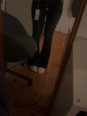 Mörkblå bootcut jeans med slitningar - Säljer ett par mörkblå bootcut jeans med snygga slitningar och kontrastsömmar. Jeansen har två knappar i midjan och klassiska fickor fram och bak. Materialet är stretchigt jeans och passformen är normal med utsvängda ben.