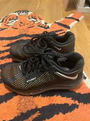 Svarta Nike x Stussy Air Max sneakers - Säljer ett par svarta Nike x Stussy Air Max sneakers med mesh-överdel och vita detaljer. Skorna har synlig Air-sula, snörning och Stussy-logga på sidan. Snygg sportig look med ventilerande material och klassisk Nike Swoosh på båda sidor.