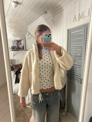 Beige teddyjacka - Supermjuk och fluffig teddyjacka från Design by amor i beige. Jackan har två stora fickor framtill, hög krage och snörning nertill för en snygg passform. Perfekt för kyliga dagar och ger en chill vibe till din outfit.