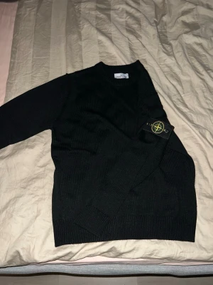 Svart stickad tröja Stone Island - Säljer en svart stickad tröja från Stone Island med klassisk patch på ärmen. Tröjan har rund halsringning, ribbade muddar och lång ärm. Perfekt för dig som gillar stilrena och tidlösa plagg med streetwear-vibe.