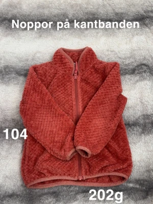 Korallfärgad fleecekofta med dragkedja - Mysig korallfärgad fleecekofta med hög krage och hel dragkedja framtill. Koftan har en fluffig, mjuk struktur och är perfekt för kyliga dagar. Passar bra till lager-på-lager och är enkel att ta på tack vare dragkedjan.🌸 Fint använt skick. Noppor på kantbanden. Storlek 104.