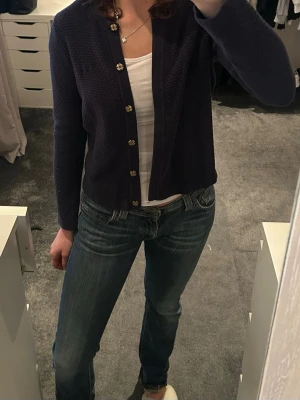 Mörkblå kofta med guldknappar - Säljer en mörkblå kofta med snygg struktur och dekorativa guldknappar framtill. Koftan har lång ärm och rak passform.