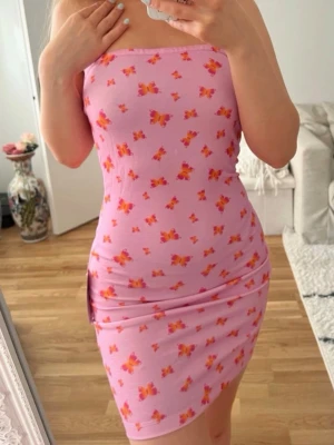 Rosa tubklänning med fjärilar NA-KD - Supersnygg ny kort bandeau klänning från NA-KD, storlek 34. Stretchigt material och har en silikonrand på insidan så den ej ska åka ner. Den är ca 67cm lång 🩷