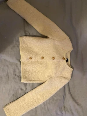 Vit bouclé kofta med guldknappar - Säljer en superfin vit ganska tjock (enlig mig), varm kofta /tröja (vet inte vad jag ska kalla den) med snygga guldfärgade knappar framtill. Materialet känns mjukt och exklusivt. Används typ 1 gång, ursprungligt pris 400kr. //skriv om ni undrar om något 💕(läs min profil)