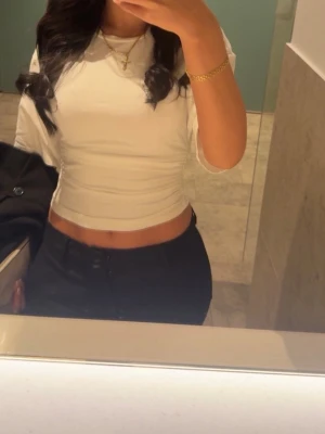 Vit croppad topp med kort ärm - Säljer en stilren vit croppad topp med korta ärmar och rund hals. Toppen har en tight passform och är perfekt att matcha med höga byxor eller kjol. Enkel och clean design utan mönster eller detaljer.