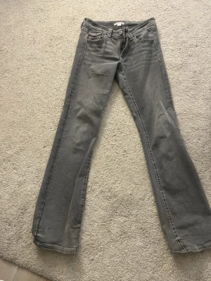 Grå bootcut jeans med fickdetaljer - Säljer ett par gråa jeans med bootcut passform och snygga fickdetaljer bak. Klassisk femficksmodell med knapp och dragkedja framtill. Jeansen har en rak men lätt utsvängd siluett och är tillverkade i mjukt jeanstyg.