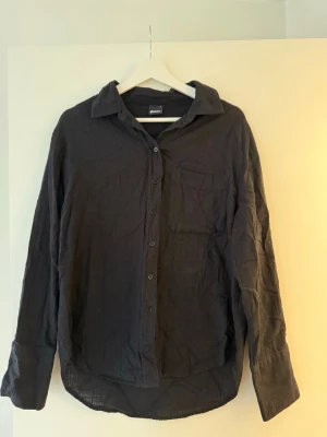 Svart linneskjorta från Gina Tricot - Svart skjorta i luftig linneblandning från Gina Tricot. Klassisk krage, bröstficka och knappar framtill. Långärmad modell med enkel, clean look som passar till allt. 