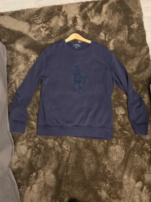 Mörkblå sweatshirt från Polo Ralph Lauren - Säljer en mörkblå sweatshirt från Polo Ralph Lauren med det klassiska broderade polospelar-märket på bröstet. Tröjan har rund halsringning och långa ärmar, perfekt för en chill och stilren look.
