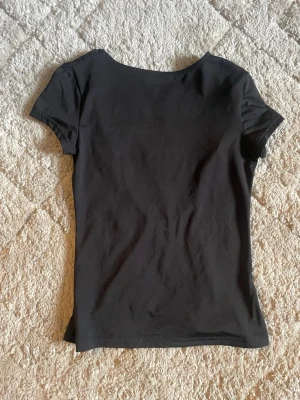 Svart topp med djup urringning - En enkel svart topp i mjukt bomullsliknande material. Toppen har korta ärmar och en riktigt djup urringning framtill som ger en snygg och modern look. Passformen är normal och tyget är stretchigt för extra komfort.