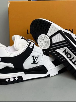 Louis Vuitton svartvita sneakers - Snygga svartvita sneakers från Louis Vuitton med tydlig LV-logga på sidan och grafiska detaljer på sulan. Skorna har snörning, platt sula och är tillverkade i skinn och syntet. Perfekta för dig som vill ha en exklusiv och trendig look.  Storlek 43 