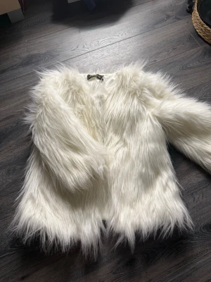 Vit fluffig pälsjacka från Lanshifei - Säljer en supermjuk och fluffig vit pälsjacka från Lanshifei. Jackan har lång luggig fuskpäls, helvit insida och stängs med hakar framtill. Perfekt för dig som vill sticka ut och hålla dig varm med stil.
