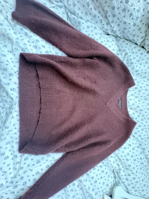 Vinröd stickad tröja - Mysig vinröd stickad tröja  i storlek XS. Tröjan har v-ringad hals och långa ärmar, med ribbade muddar vid hals, ärmslut och nederkant. Perfekt för att hålla sig varm under kyliga dagar och har en enkel, klassisk look.