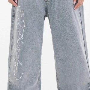 Ed Hardy relaxed wide jeans med strass - Säljer ett par ljus blåa relaxed fit jeans från Ed Hardy med breda ben och strassdetaljer längs ena benet samt  bakfickorna. Använd max 2 gånger, säljer då dem är för stora för mig