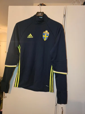 Svenska landslaget långärmad Adidas S - Mörkblå långärmad fotbollströja från Adidas med Svenska Fotbollsförbundets emblem på bröstet och gula Adidas-ränder längs sidorna. Tröjan har tumhål vid ärmslut och är tillverkad i Climacool-material som andas. Perfekt för träning eller match.