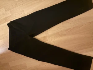 Svarta mjukisbyxor/kostymbyxor Jack & Jones S - Svarta mjukisbyxor/ kostymbyxorfrån Jack & Jones med elastisk midja och snörning. Byxorna har en rak passform och är gjorda i mjukt material som är perfekt för chill dagar. Snyggt minimalistisk design utan synliga loggor på benen.