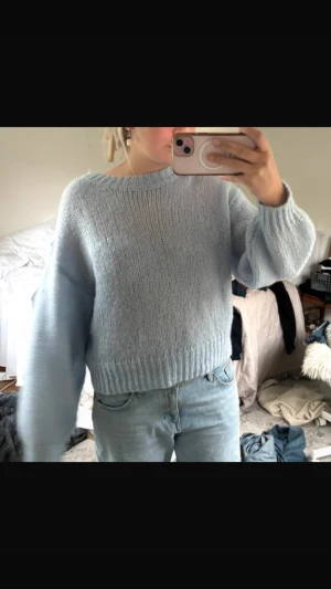 Ljusblå stickad tröja med loose fit - Mysig ljusblå stickad tröja med bred ribbad kant nertill och vid ärmslut. Tröjan har en loose passform och långa ärmar, perfekt för lager på lager. Enkel och stilren design som är lätt att matcha med jeans eller kjol.