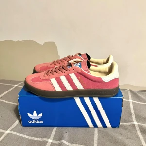 Rosa Adidas Gazelle - Säljer ett par snygga rosa adidas gazelle. De är i mycket bra skick utan någon defekt. Storlek 43 1/3 men är som vanligt 43. Skolådan ingår ej tyvärr.