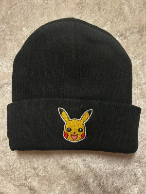 Pikachu mössa svart och vinröd - Två snygga mössor med Pikachu broderat framtill. Ena är svart och andra vinröd, båda i mjukt stickat material med uppvikt kant. Perfekt för dig som vill visa din Pokémon-stil och hålla dig varm. Pikachu-detaljen är broderad i gult, rött och svart. 99kr/st helt ny 