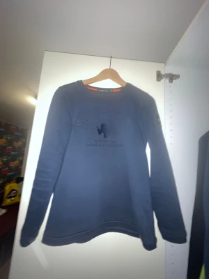 Blå Sail Racing sweatshirt - Snygg marinblå sweatshirt från Sail Racing med broderad logga på bröstet och patch på ärmen med texten 'Sail Antarctica Expedition'. Tröjan har rund hals, långa ärmar och är gjord i mjuk bomullsmix. Perfekt för dig som gillar äventyr och stil.