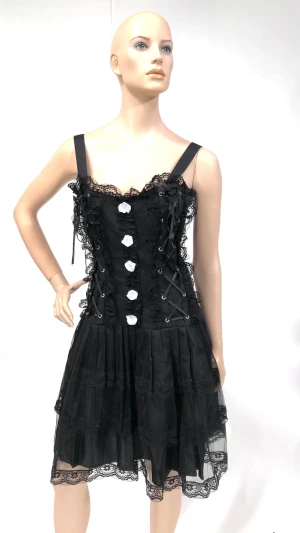 Svart klänning med spets och knappar - Snygg svart klänning med spetsdetaljer och vita knappar framtill. Klänningen har smala axelband och en volangkjol som ger en lekfull look. Perfekt för en kväll ute eller en speciell tillställning.