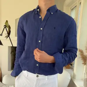 Snygg blå skjorta i 100% linne från Morris Stockholm. Klassisk button-down krage, vita knappar och diskret broderad logga på bröstet. Perfekt för dig som gillar en stilren och luftig look under varmare dagar.