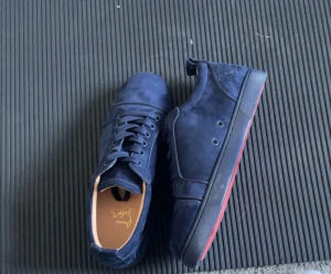 Mörkblå sneakers från Christian Louboutin - Snygga mörkblå sneakers från Christian Louboutin med röd detalj på sulan. Skorna har rund tå, snörning och är tillverkade i mocka med en lyxig känsla. Innersulan är i skinn med guldtext och yttersulan har Louboutin-logga. Perfekt för dig som gillar exklusiva sneakers.