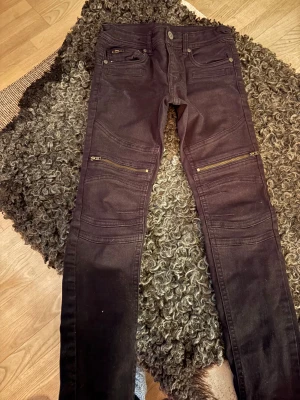 Svarta jeans med dragkedjor från Lindex - Svarta jeans från Lindex med coola detaljer som dragkedjor vid knäna och flera fickor fram. Jeansen har en slim passform och är tillverkade i stretchig bomull för skön känsla. Perfekt för dig som gillar en edgy stil och vill ha något som sticker ut.