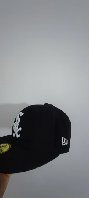 Chicago White Sox svart New Era keps - Svart New Era 59FIFTY keps med vit Chicago White Sox-logga framtill och broderad text 'Greetings from Chicago' samt grönt och vitt Southside-märke på sidan. Klassisk flat peak och broderade detaljer. Perfekt för dig som gillar streetwear och sport.