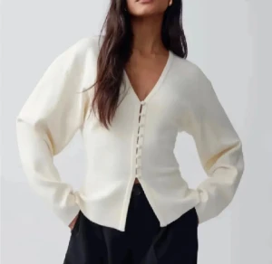 Vit kofta med v-ringning från Gina Tricot - Snygg vit kofta från Gina Tricot med v-ringad hals och dekorativa knappar framtill. Modellen är lite croppad och har långa ärmar. Mjuk stickad känsla som passar perfekt till svarta jeans eller kjol. Enkel och stilren design som är lätt att matcha.