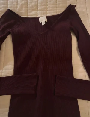 Mörkröd ribbad långärmad tröja XS - Snygg mörkröd ribbad tröja från H&M med v-ringad hals och lång ärm. Modellen är tight och har en offshoulder-look som ger en trendig vibe. Perfekt för dig som gillar stilrena och enkla plagg med en twist.