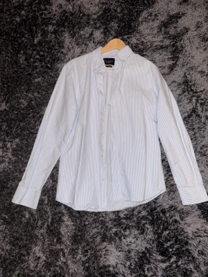 Randig skjorta från Bondelid - Snygg skjorta från Bondelid i ljusblått och vitt med smala ränder. Klassisk button-down krage och långa ärmar med manschett. Skjortan har en normal passform och är gjord i mjuk bomull, perfekt för en clean och fräsch look.