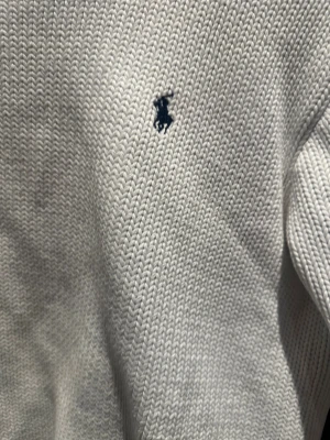 Vit stickad tröja från Ralph Lauren - Vit stickad tröja från Ralph Lauren med klassisk marinblå logga broderad på bröstet. Rund halsringning med ribbad kant och ribbade muddar vid ärmslut och nederkant. Perfekt för dig som gillar clean och stilren look.