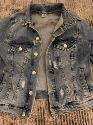 Ljusblå jeansjacka från &Denim - Säljer en snygg ljusblå jeansjacka från &Denim med slitna detaljer och klassiska bröstfickor med knappar. Jackan har långa ärmar, silverfärgade knappar och kontrastsömmar. Perfekt för dig som vill ha en cool och avslappnad stil. Priset går att diskutera 💕