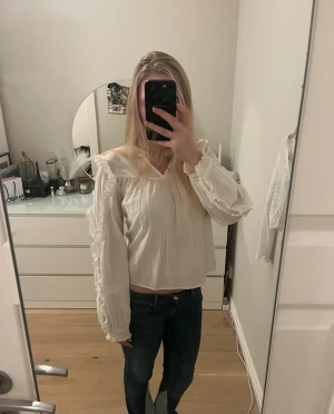 Vit blus med volangdetaljer - Säljer en söt vit blus från Gina tricot med volanger längs axlar och ärmar. Blusen har långärmad design, lätt v-ringad hals och är gjord i mjuk bomull. Perfekt för dig som gillar romantisk och chill stil. Passar dig som vill ha en loose fit och gillar detaljer. Storleken är 158/164 men passar som en S💕