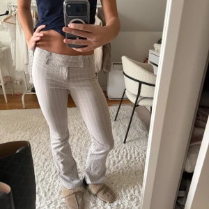 Lågmidjade bootcut kostymbyxor  - Snygga beige kostymbyxor med vita ränder och bootcut-snitt. De har låg midja med dubbla knappar fram till och snedknäppe! Väldigt stretchigt och skönt material. 