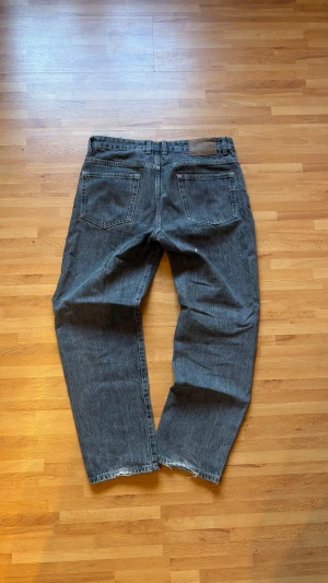 mörkgrå jeans från Bull&Bear Straight fit  - Säljer ett par mörkgrå jeans från Pull&Bear Straight fit. Jeansen har fem fickor, knappgylf och råa kanter vid bensluten för en avslappnad vibe. Passar dig som gillar lite loose och tidlös stil. På bild 5 så ser ni att byxorna har ett litet hål baktill, men det syns knappt när man har på sig dem! 