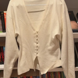 Vit kofta med v-ringning och knappar - Snygg vit kofta med djup v-ringning och dekorativa knappar framtill. Koftan har lång ärm och är tillverkad i ett mjukt stickat material som känns skönt mot huden. Perfekt för dig som gillar stilrena och enkla plagg med en twist. Lagom i storlek passar mig som är 175. Lite nopprig.