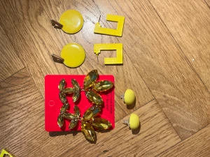 Fyra par coola örhängen i gult - Säljer fyra par örhängen i olika former och stilar. Ett par stora runda i blank gul plast, ett par kantiga fyrkantiga i gul plast, ett par små runda i matt gul och ett par glittriga med stora gula stenar i bladform. Perfekt för dig som gillar färg och statement-smycken.