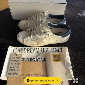 Golden Goose - Golden Goose super star Klassisk låg modell med snörning och platt sula storlek 41. Snyggt slitna detaljer för den ikoniska looken. Perfekta för dig som gillar trendig stil och exklusiva märken. Skorna är köpta nya på golden goose hemsida men tyvärr fått lite slitage pågrund av användning. Hör av dig vid fler frågor och pris kan diskuteras.