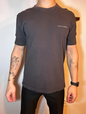 Svart/grå t-shirt från Tiger of Sweden - En stilren svart t-shirt från Tiger of Sweden med diskret logga på bröstet. Klassisk passform med rund halsringning och korta ärmar. Tillverkad i mjuk bomull som känns skön mot huden. Perfekt för en clean och enkel look.