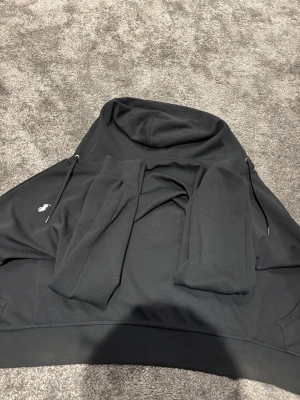 Svart hoodie från Polo Ralph Lauren XS - Svart hoodie från Polo Ralph Lauren i storlek XS. Tröjan har dragkedja framtill, huva med snörning och den klassiska vita Polo-loggan broderad på bröstet. Tillverkad i mjuk bomull, perfekt för chill dagar. Långärmad och stilren design. 