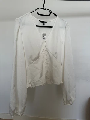 Vit blus Kappahl - Säljer en vit blus från KappAhl i storlek 42. Blusen har v-ringning, långa ärmar med resår vid ärmslut och dekorativa tygklädda knappar framtill. Smockad och volangkantad nederdel baktill  Obs: Alla plagg säljs endast fram till 28/12 