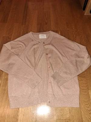 Glittrig rosa kofta från Zara - Snygg rosa glittrig kofta från Zara. Koftan har långa ärmar, ribbade muddar och knappar framtill. Perfekt för dig som gillar lite extra shimmer i vardagen. Två  fickor framtill.